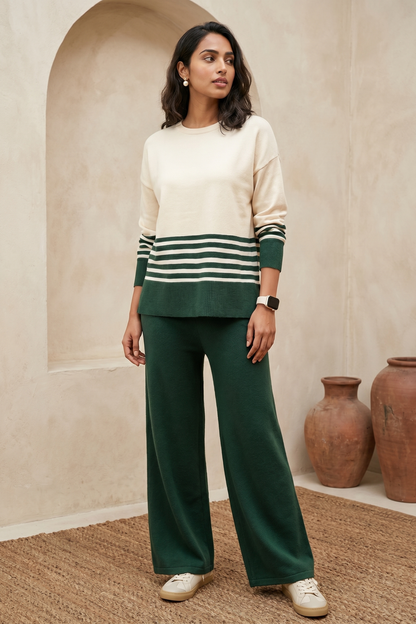 Woman wearing a cream and green striped sweater with green pants in a room with beige walls and brown rugs.